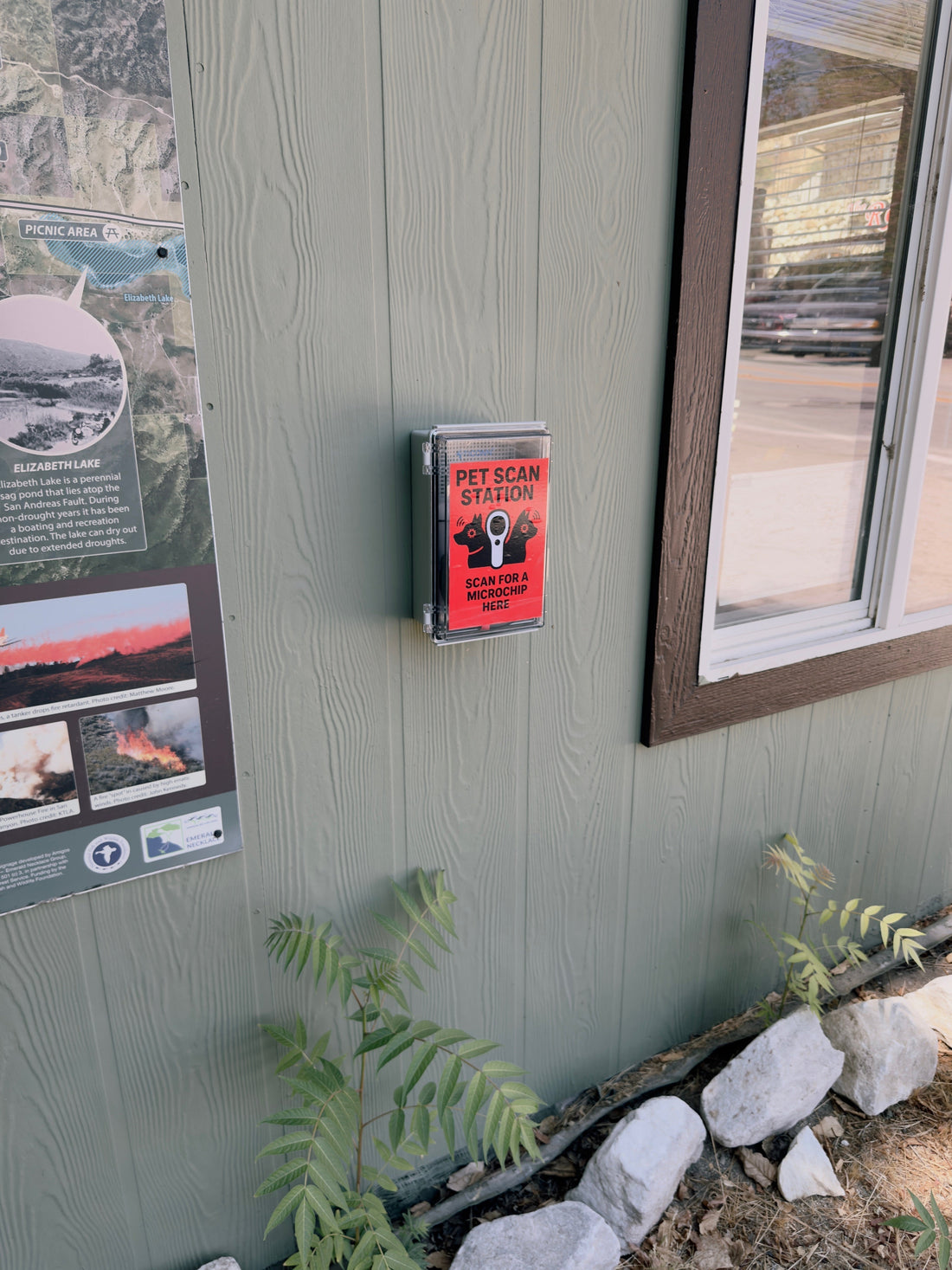 Photo of the Pet Scanner box affixed to the outside wall of the building  with a window on the right and a map on the left.